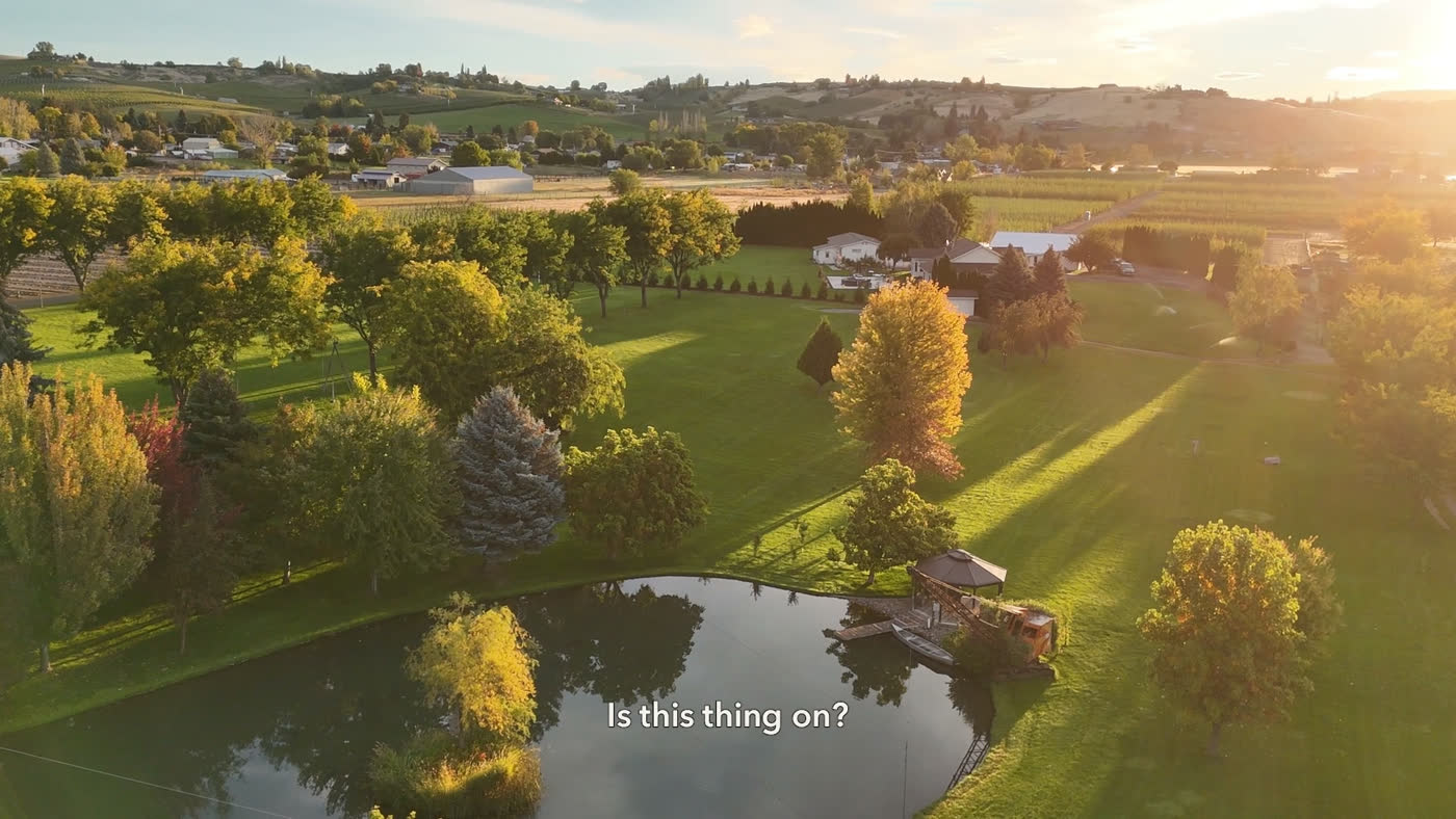 Aerial view of a farm at golden hour, a pond and trees, with the caption “Is this thing on?”