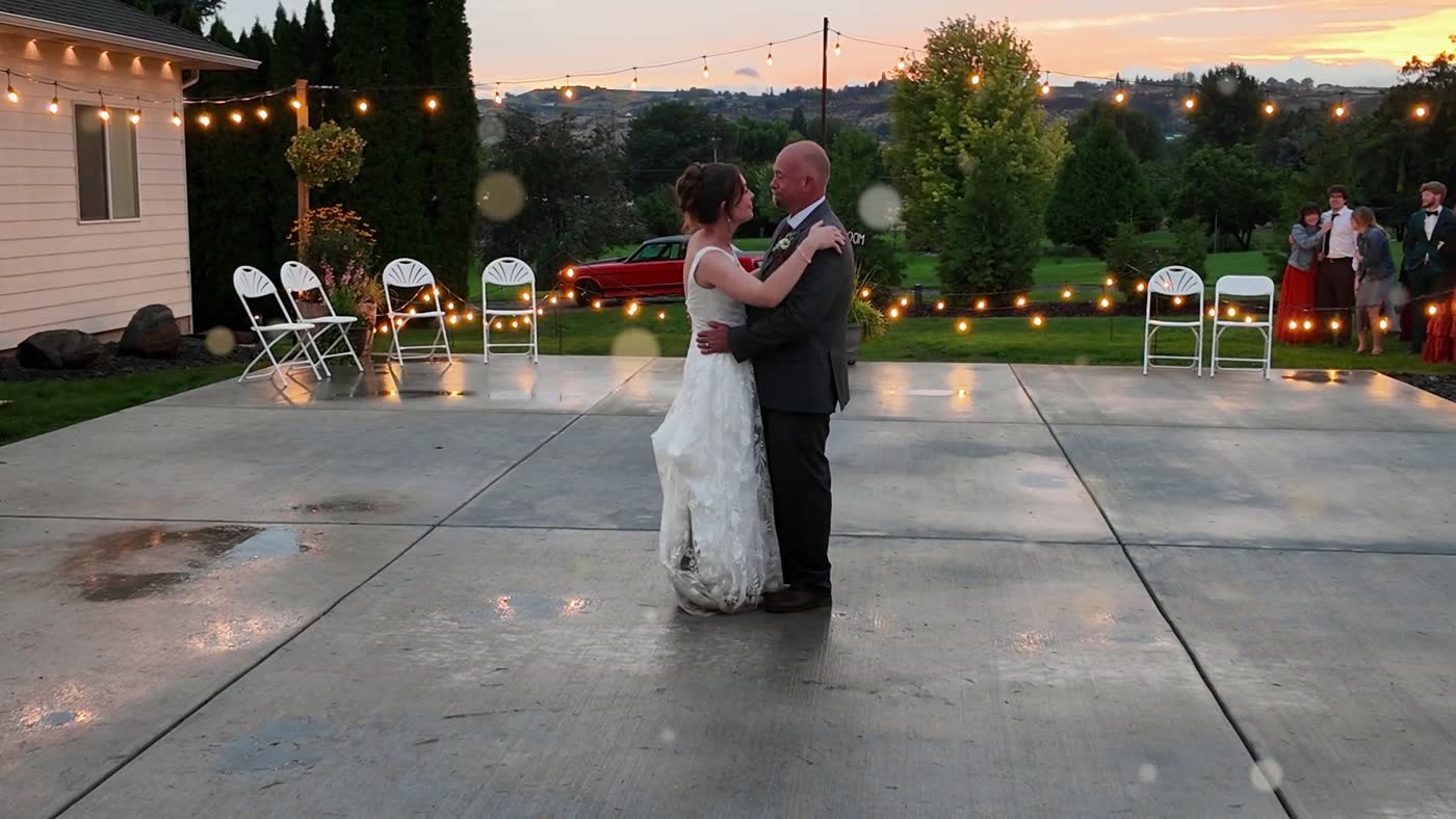 The bride dances with her father on the patio as evening falls