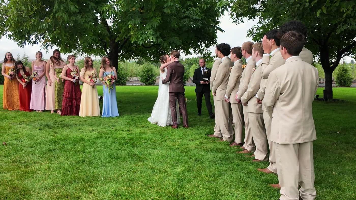 The couple kiss under the tree between the bridesmaids and groomsmen