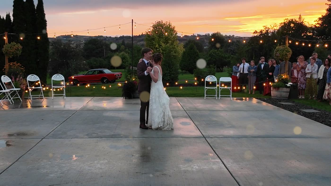 A couple's first dance on a wet patio under string lights at sunset